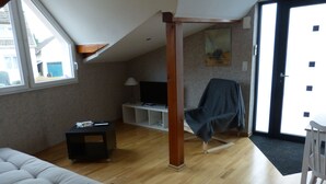 Habitación con cama tipo litera, un televisor sobre un mueble blanco, una silla con una manta y una puerta que da al exterior.