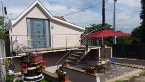 Un edificio moderno con techo inclinado, una escalera que lleva a un balcón y mobiliario exterior con una sombrilla roja.