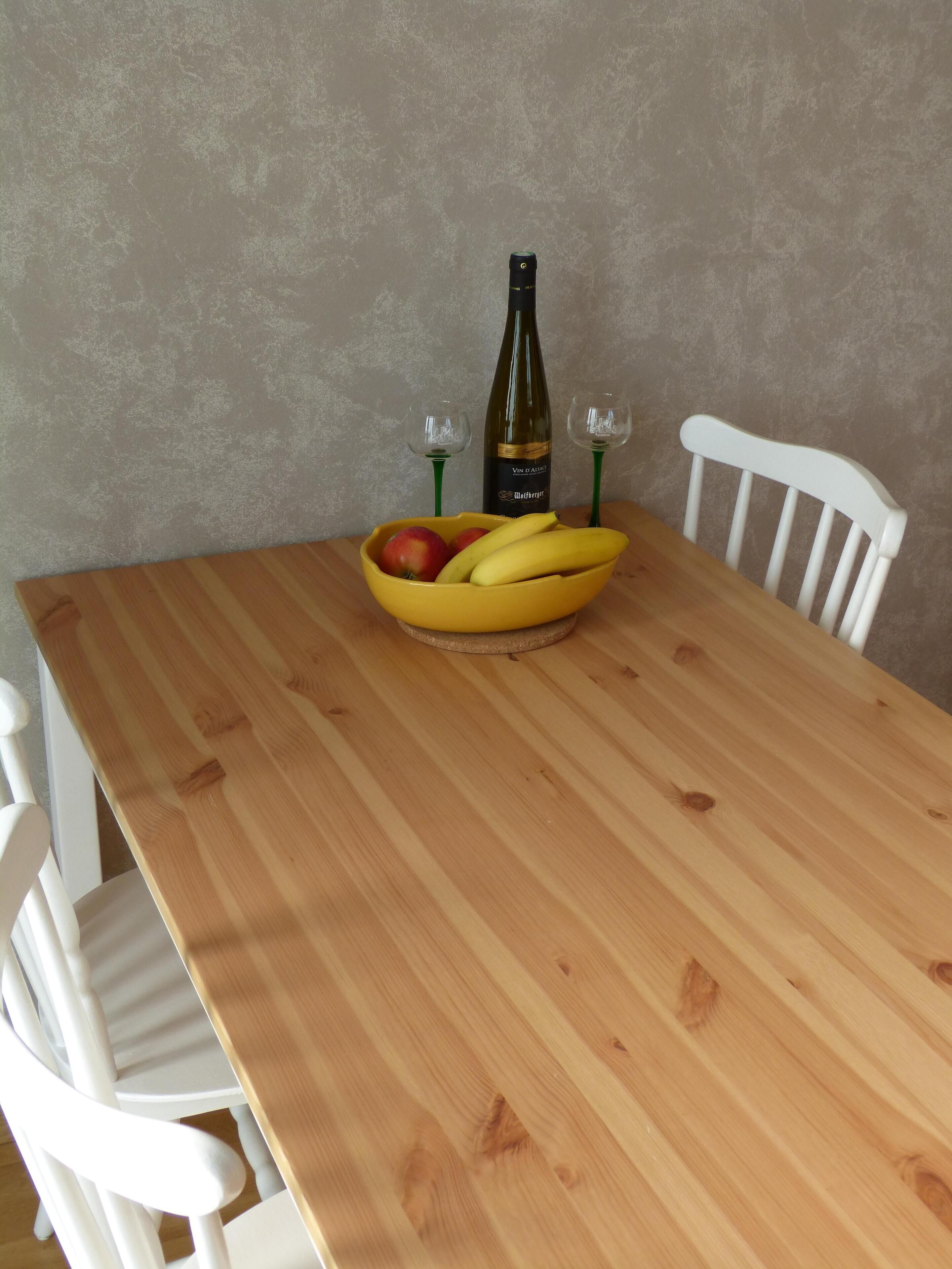 A wooden dining table with a bowl of fruit and a bottle of wine.