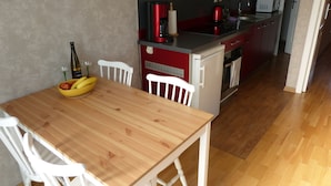 Una cocina compacta con comedor, que incluye una mesa de madera, sillas blancas y un refrigerador rojo.