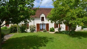 A two-story house with a red-tiled roof, a small balcony, and a front door with wooden shutters.