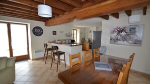 A dining area with a wooden table and chairs, a kitchen in the background, and a bicycle painting on the wall.