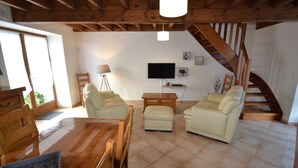 A spacious living room with a wooden ceiling, a staircase, a TV, and a dining area with a wooden table and chairs.