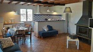 Un saló acollidor amb un sofà, una taula de menjador i cadires. Hi ha una zona de cuina amb una placa de cocció i una finestra.
