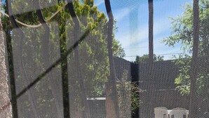 A view through a window with a metal screen, a brick ledge, and a fenced outdoor area with a bench and a small table. - SUNNY HOME / STUDIO ALL EQUIPPED (Cuges-Les-Pins)