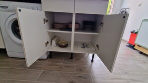 A kitchen with a built-in washing machine, open cabinets with dishes and kitchenware, and a red trash bin. - SUNNY HOME / STUDIO ALL EQUIPPED (Cuges-Les-Pins)