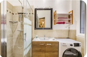 Une salle de bain moderne dotée d’une cabine de douche en verre, d’un lavabo intégré, d’un miroir et d’un lave-linge à chargement frontal.