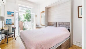 Una camera da letto con un letto, una scrivania e una sedia. Si vede una finestra e un'uscita che dà su uno spazio all'aperto.
