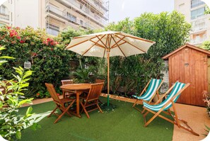 Une terrasse avec une table et des chaises en bois, une chaise longue à rayures et un grand parasol.