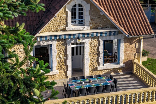 A stone building with a tiled roof, a balcony with a railing, and a table set for dining. - Gite Les Bleuets - 12 pers. for get-togethers, near golf course (Saint-Geyrac)