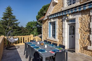 Een stenen gebouw met een balkon, een eettafel gedekt met borden, glazen en een hangstoel.