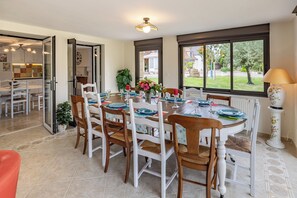 A dining area with a round table set for six, surrounded by white chairs with woven seats. - Gite Les Bleuets - 12 pers. for get-togethers, near golf course (Saint-Geyrac)