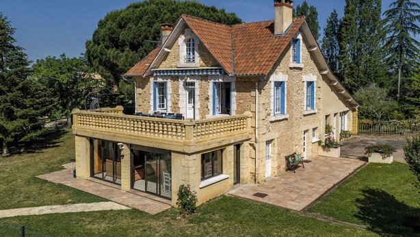 Une maison en pierre à deux étages, dotée d’un balcon, d’une terrasse couverte et d’un jardin.