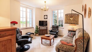 Un salon comprenant un canapé, des fauteuils, un téléviseur, une table basse et un lustre.