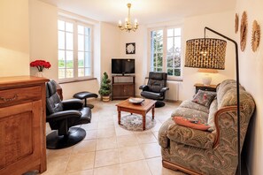 A living room with a sofa, chairs, a television, a coffee table, and a chandelier. - Gite Les Bleuets - 12 pers. for get-togethers, near golf course (Saint-Geyrac)