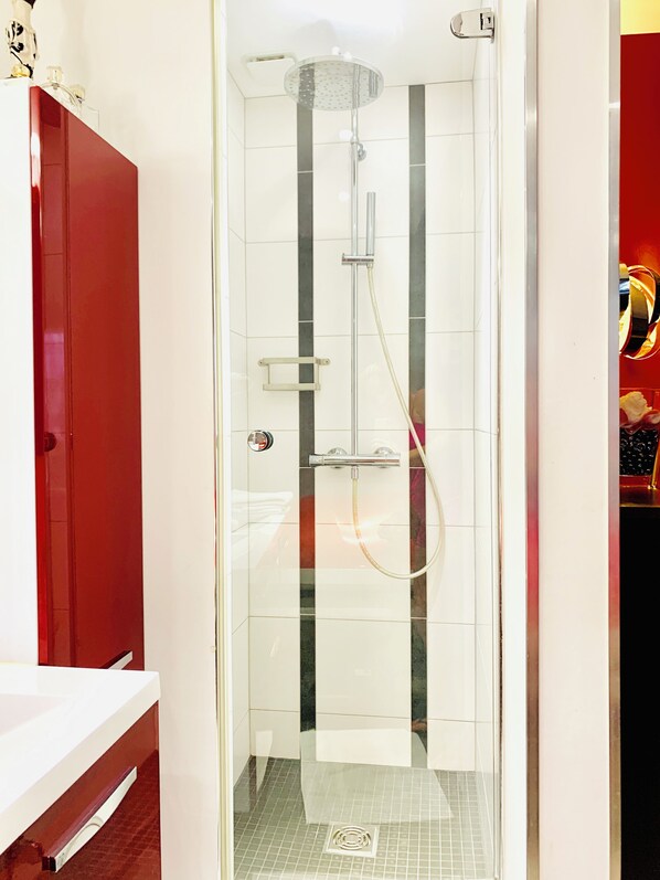 A glass-enclosed shower with a handheld showerhead and a wall-mounted faucet.