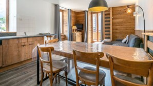 A modern kitchen with wooden cabinets, a dining table, and chairs. There is a large window providing natural light and a view of the outdoors.