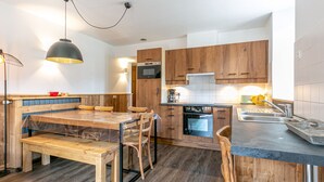 A modern kitchen with wooden cabinets, a built-in oven, and a dining area with a bench and chairs.