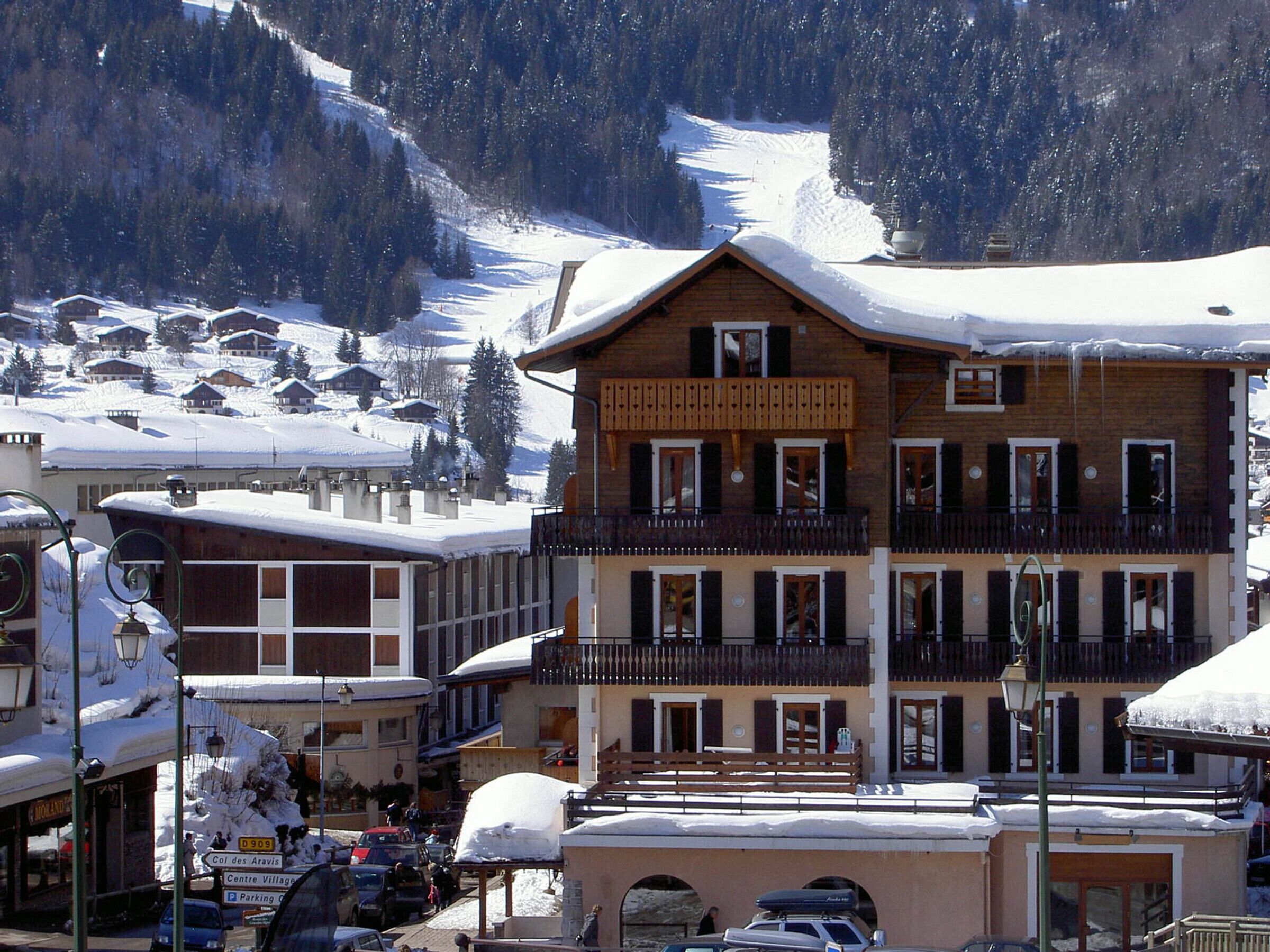 A multi-story building with balconies, a snow-covered roof, and a mountainous backdrop.