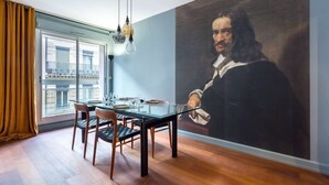 A dining area with a glass table, chairs, and a large portrait on the wall. - Stella - Furnished apartment - Downtown Lyon (Lyon)
