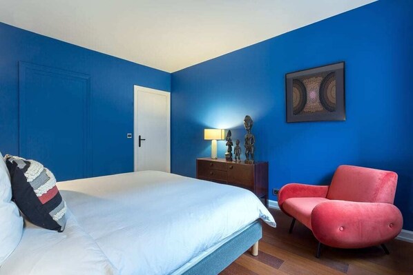 Un dormitorio con una cama, una silla roja, un tocador y una puerta.