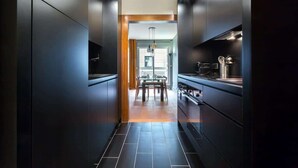 A modern kitchen with dark cabinetry, a central island, and a dining area with a chandelier. - Stella - Furnished apartment - Downtown Lyon (Lyon)