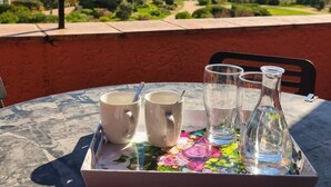 A table with a tray holding two mugs, a glass, and a bottle, set against a scenic view of a coastal landscape. - MARINES DE GASSIN : 2-BEDROOMS APARTMENT WITH CABIN IN A RESIDENCE IN FRONT OF THE SEA WITH POOL (GASSIN)