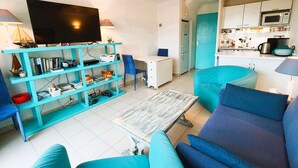 A living room with a TV, bookshelf, and blue furniture. - MARINES DE GASSIN : 2-BEDROOMS APARTMENT WITH CABIN IN A RESIDENCE IN FRONT OF THE SEA WITH POOL (GASSIN)