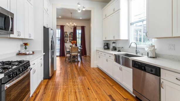 A modern kitchen with white cabinets, stainless steel appliances, and a wooden floor.