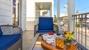 A balcony with wicker furniture, a tray with coffee cups, pastries, and flowers.