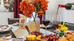 A table set with cheese, grapes, a bottle of red wine, and a vase of orange flowers.