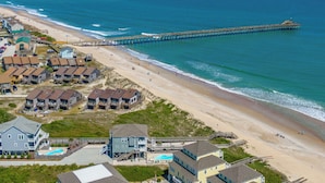 Een kustgebied met een pier die in de zee uitloopt, strandwoningen en een zwembad.