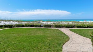 Ein gepflasterter Weg führt zu einem Strand mit klarem, blauem Wasser.