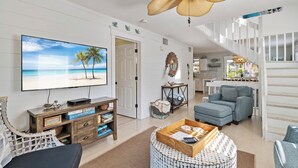 Ein Wohnzimmer mit Fernseher, Sofa, Hocker und Deckenventilator.