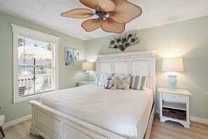 A bedroom with a bed, a ceiling fan, a window with blinds, and two bedside tables with lamps.