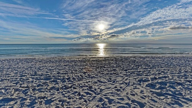 Ein Strand mit blauem Himmel und der Sonne, die sich im Wasser spiegelt.