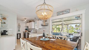 Eine Küche mit einem Holztisch, weißen Stühlen, einer Chandelier und Blick ins Freie.