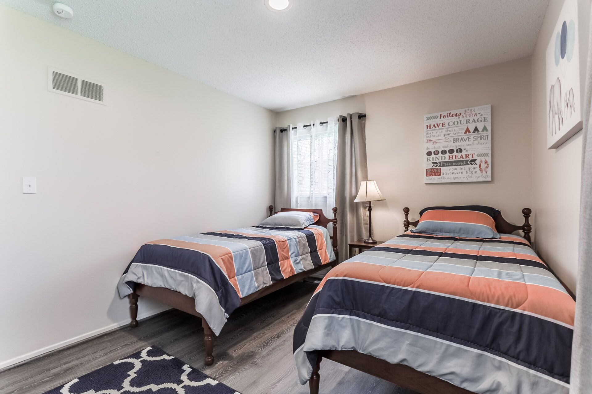 A bedroom with two beds, a window with curtains, a wall clock, and motivational posters.