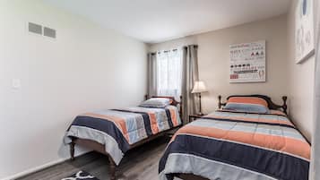 A bedroom with two beds, a window with curtains, a wall clock, and motivational posters.