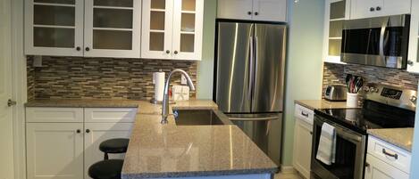 A modern kitchen with white cabinets, a stainless steel refrigerator, a microwave, and an oven.