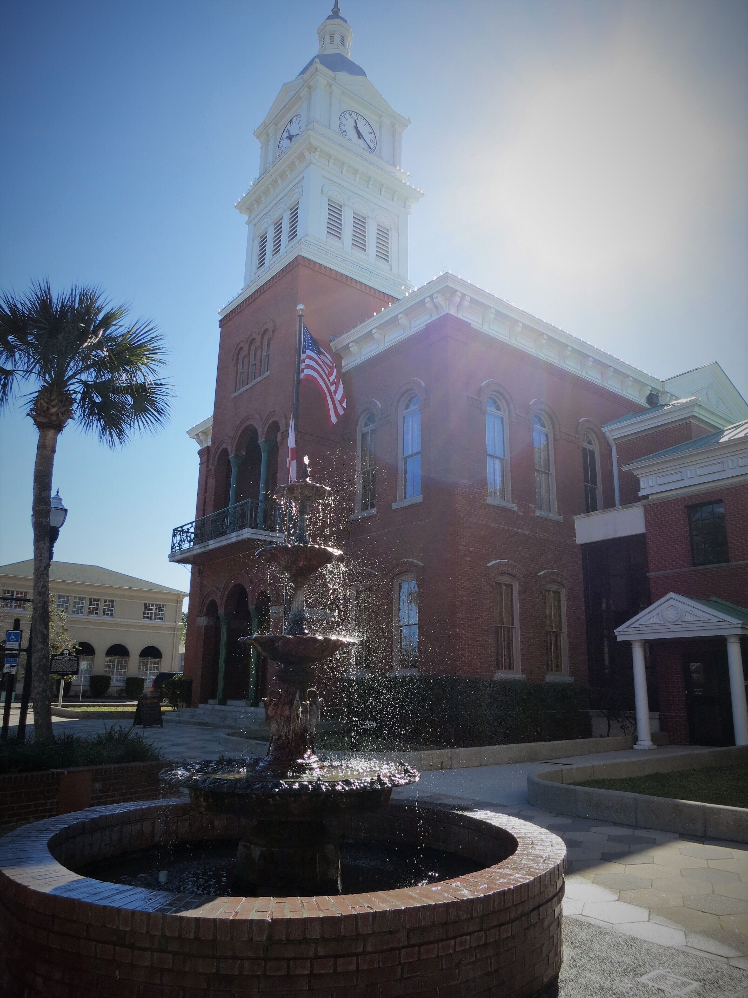 A historic building with a clock tower, a fountain, and an American flag.