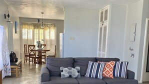 Una sala de estar con un sofá gris, alfombra estampada y un comedor con una mesa y sillas.