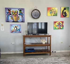 A living room with a TV on a wooden stand, surrounded by colorful abstract paintings.