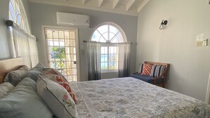 Un dormitorio con una cama grande, cabecera de madera, ventana con cortinas, ventilador de techo y equipo de aire acondicionado.