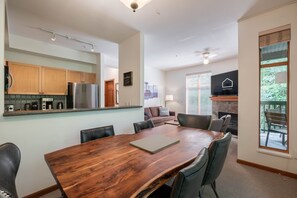 A modern kitchen with stainless steel appliances, a dining area with a wooden table and leather chairs, and a living area with a sofa and a fireplace.