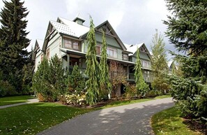 A large, multi-story house with a prominent front porch and a driveway leading to the entrance.