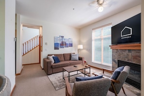 A living room with a sofa, coffee table, and armchair, a fireplace, a TV, and a staircase leading to another room.