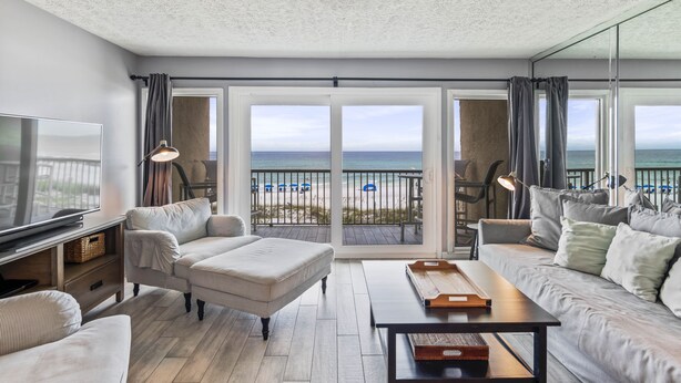 A modern living room with a large TV, comfortable seating, a wooden coffee table, and a view of the beach through large sliding doors. - EMERALD COAST PARADISE! 202 Destin Seafarer (Destin)