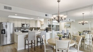 Een moderne keuken met witte kasten, roestvrijstalen apparatuur, een centraal eiland met zitplaatsen en een kroonluchter.