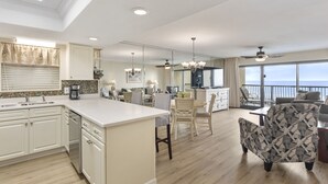 Een ruime keuken met een centraal eiland, een eethoek met stoelen en uitzicht op de oceaan door grote ramen.